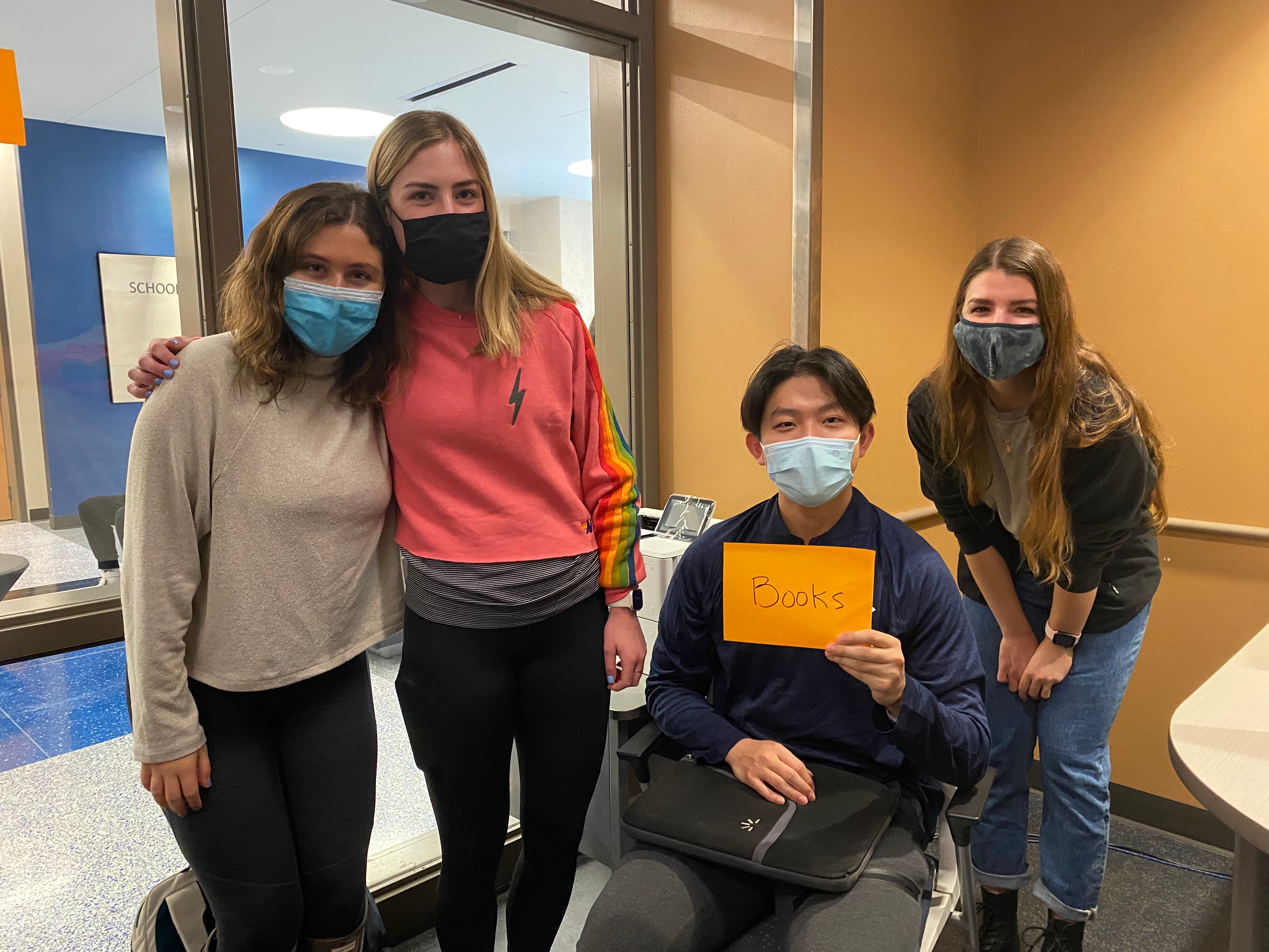 Four students standing next to each other holding a sign that says Books