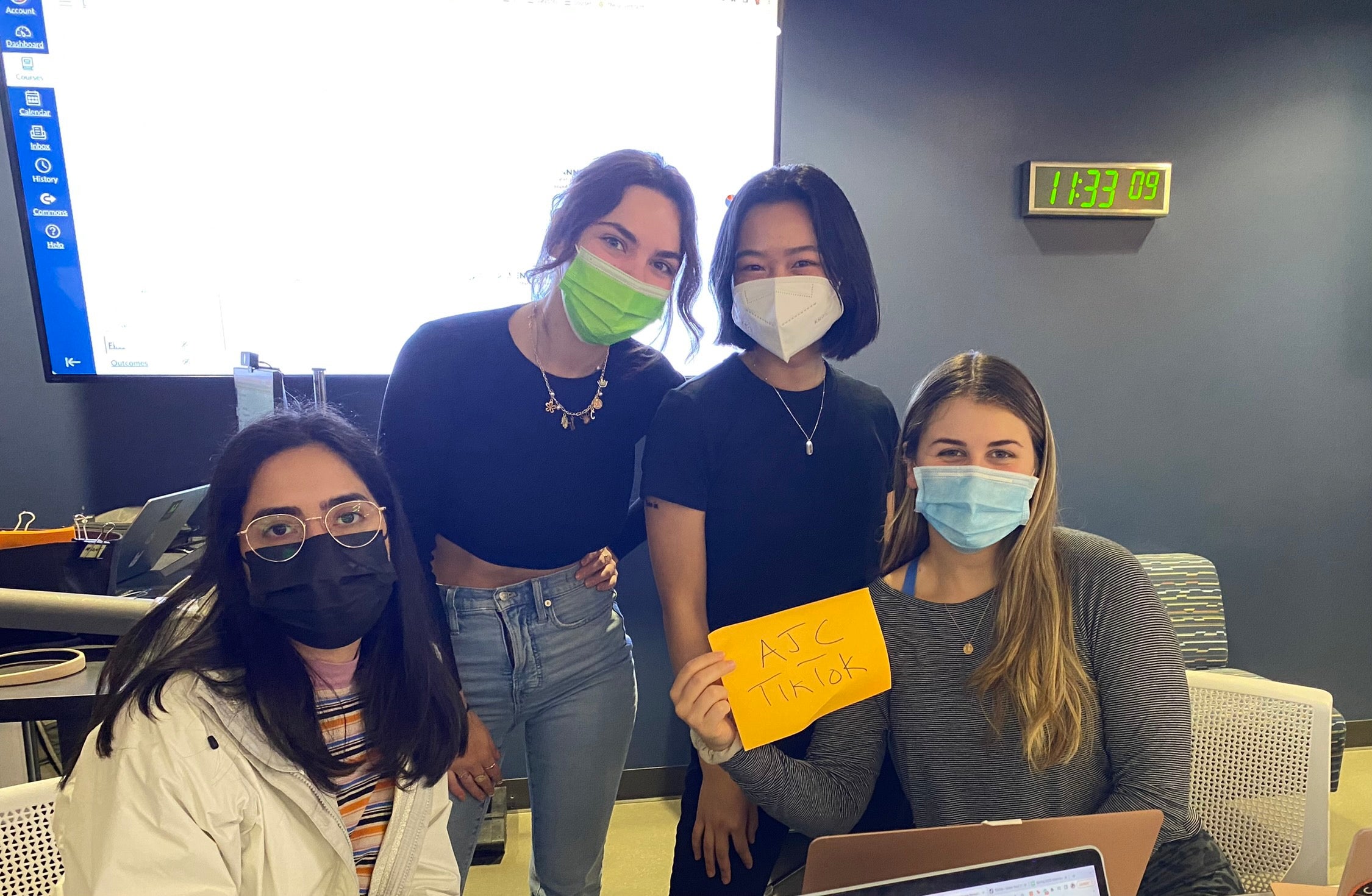 Four students stand next to each other holding up a sign that says "AJC TikTok"