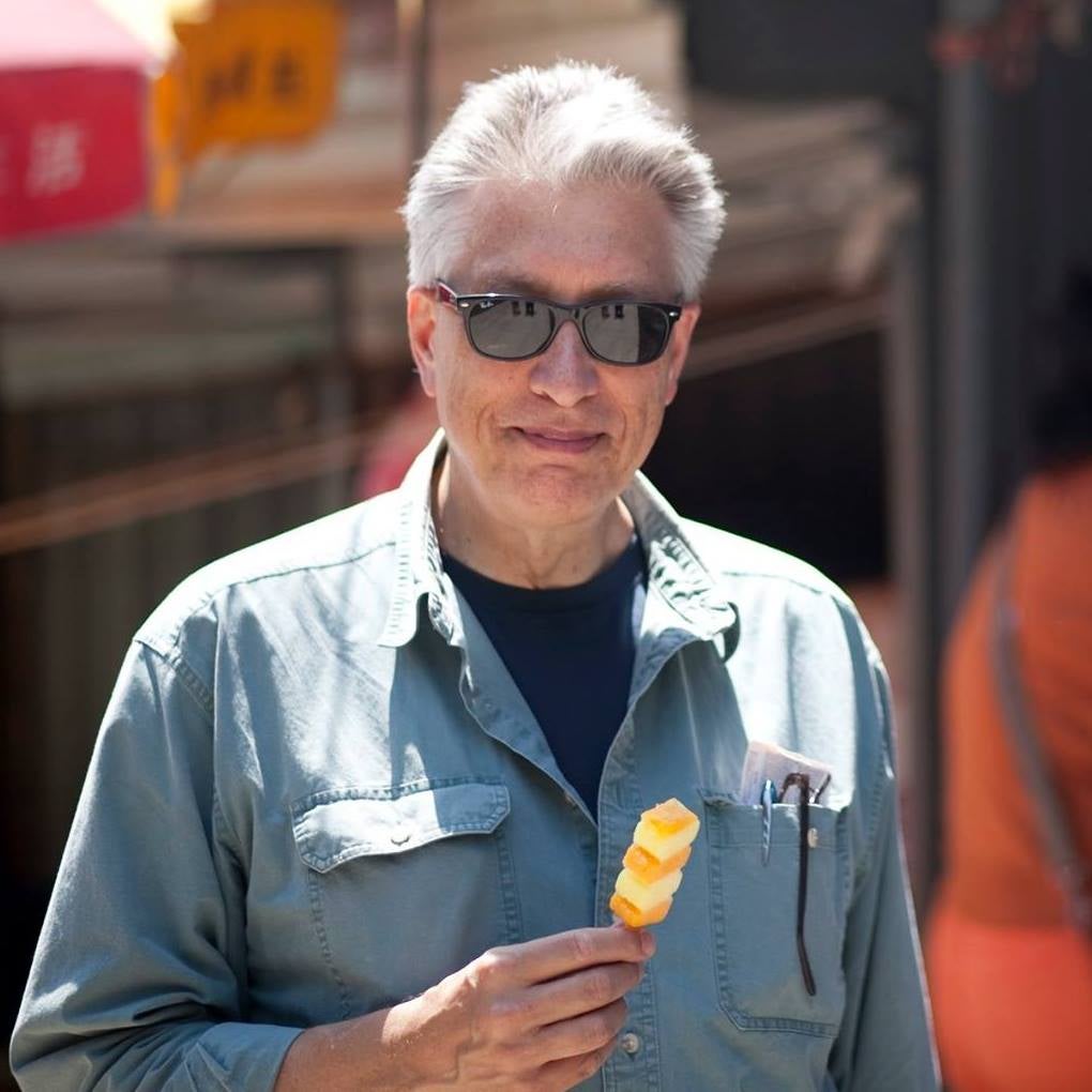 Tracy Dahlby stands smiling, holding food in his hand