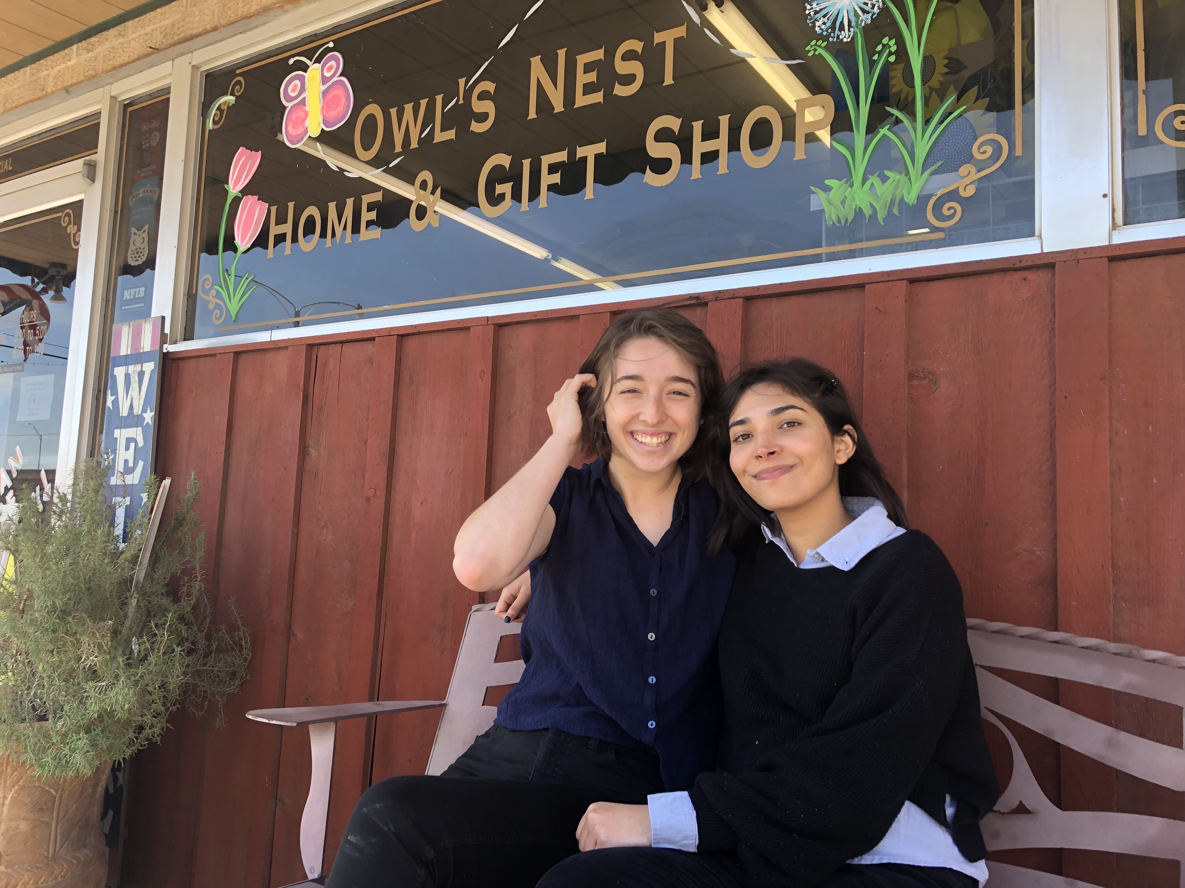 Tinu and Haley sit on a bench in front of a storefront
