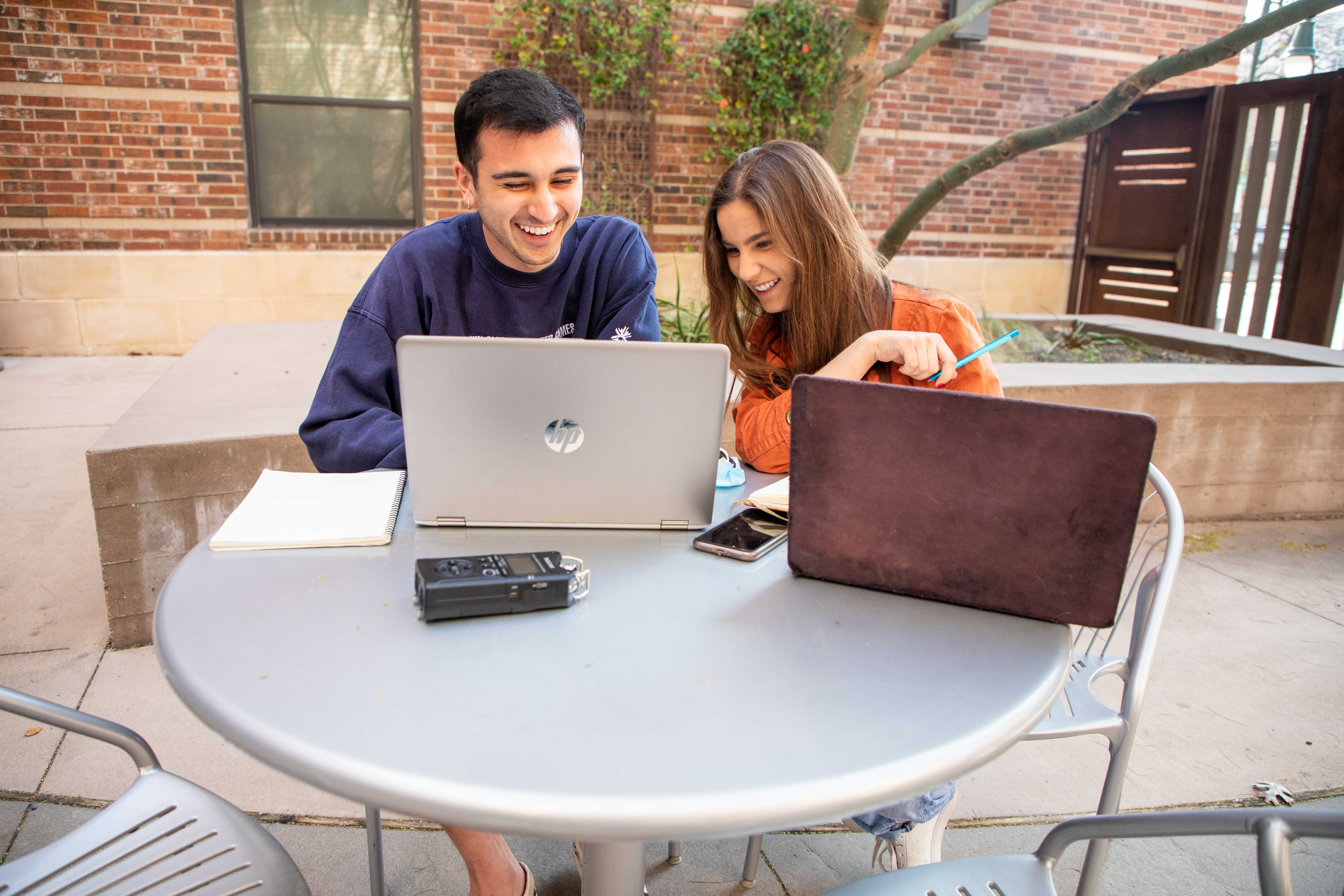 Ashley Miznazi and Kenny Jones work on their podcast at a patio table.