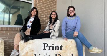 students sitting on rock that reads "Print Ain't Dead"
