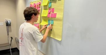 student putting sticky notes on wall