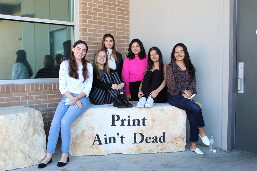 six students sit on a rock that says "Print Ain't Dead"