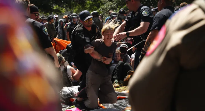 A person is carried by police officers in a crowd.